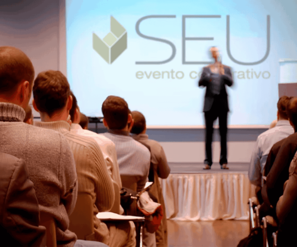 Fotos para artigos antigos (43) Público acompanhando palestra em um auditório corporativo, com apresentação no palco representando um evento bem-sucedido.